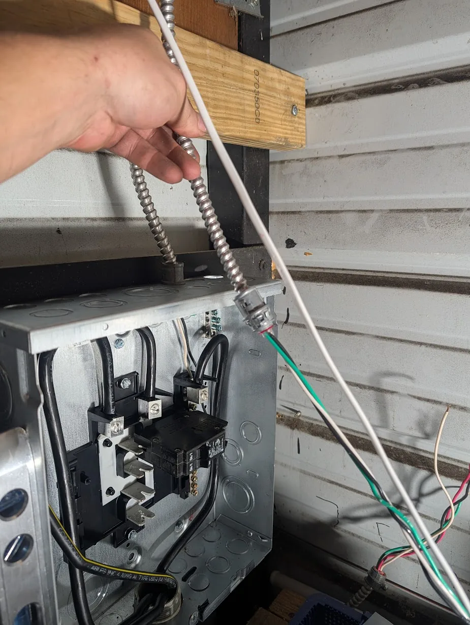 Hand pulling an MC whip through a new knockout in the shed panel