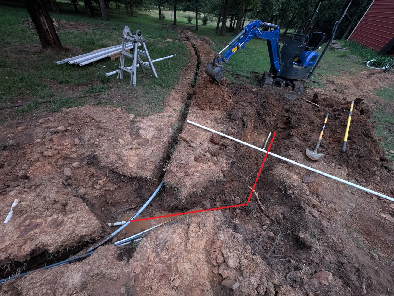Excavated trench with a red line traced over where the buried water line actually turns 45° and runs downhill