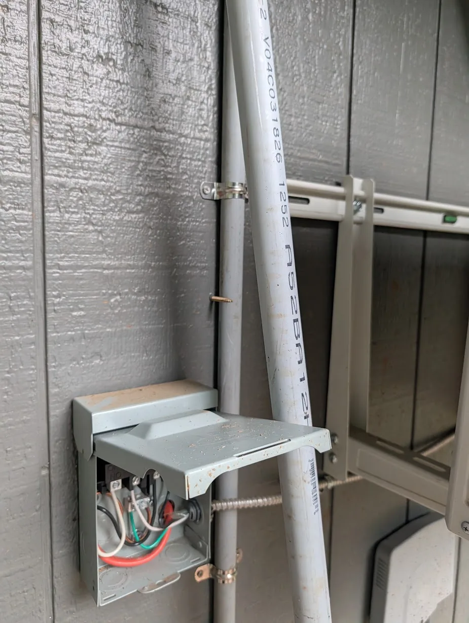 Outside of the house showing the mini-split disconnect and refrigerant line set right where the new conduit needs to come through