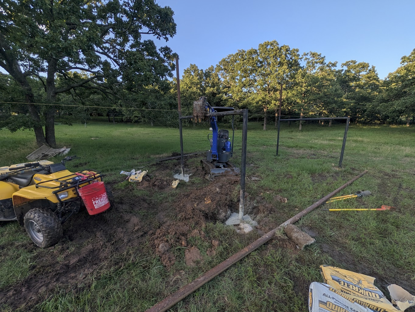 Mini excavator holding a post plumb while the concrete sets
