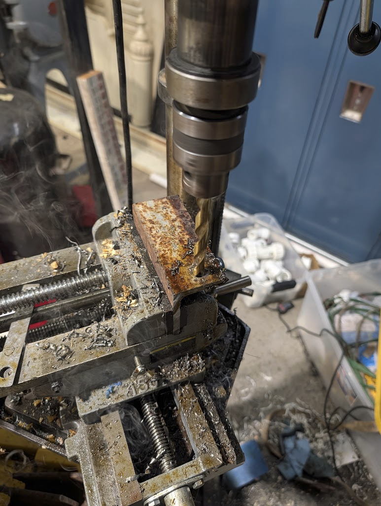 Drill press cutting through angle iron with cutting oil smoking off the bit
