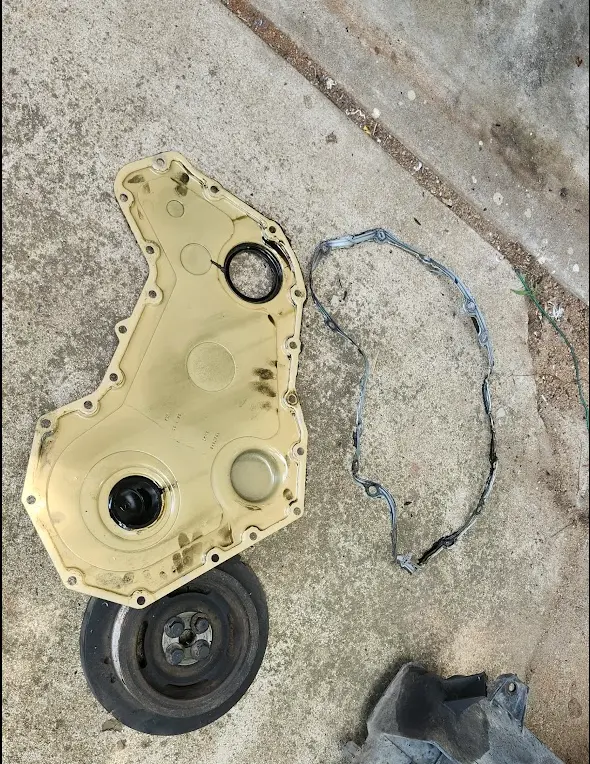 Picture of the crank pulley and timing cover sitting on the ground, removed.